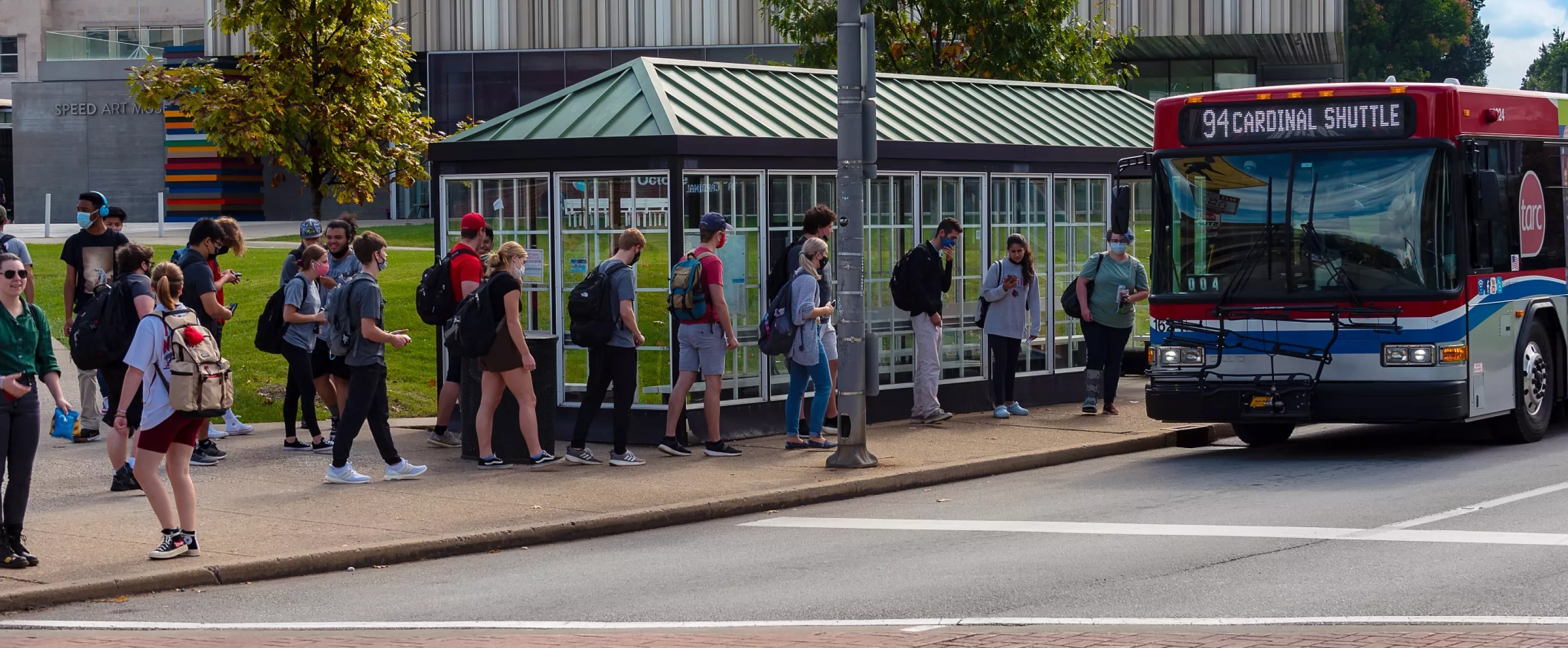 Students waiting for a Cardinal Shuttle with the Speed Art Museum in the background